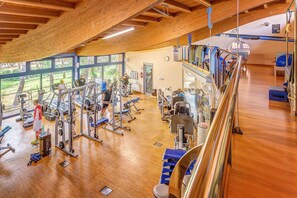A gym with wooden floors, various exercise equipment, and large windows offering views of the outdoors. - Hotel with private beach in San Vincenzo (San Vincenzo)