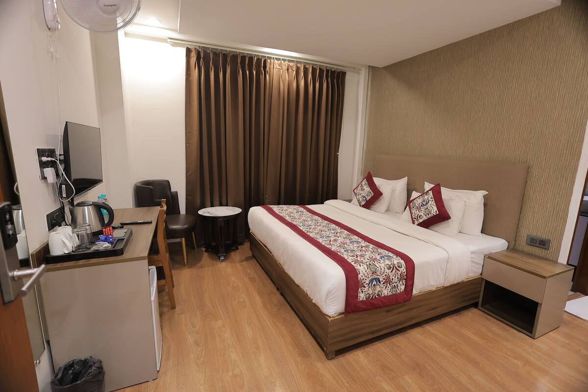 A hotel room with a bed, a desk with a computer, a small table, and a trash bin.