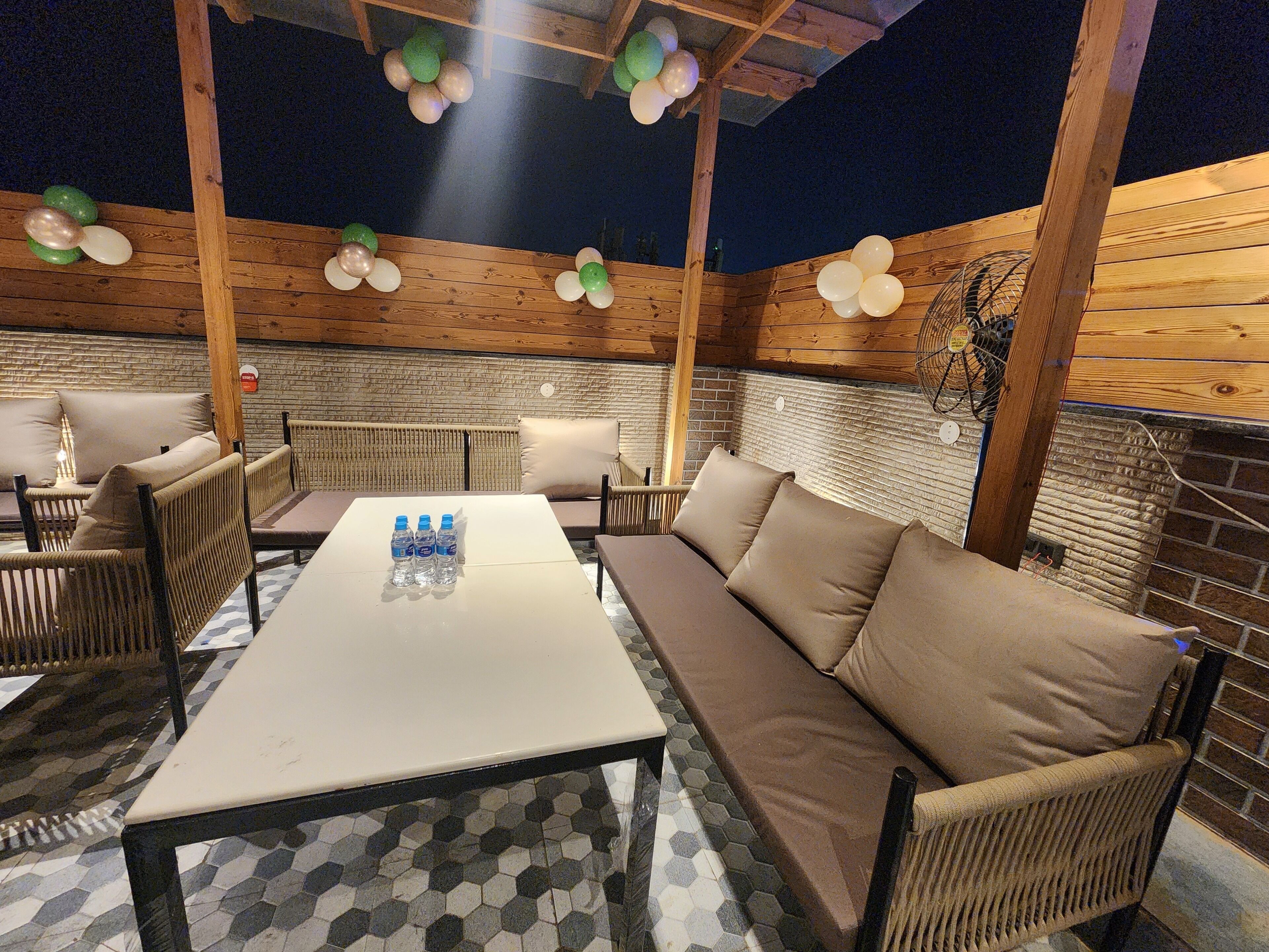 Eine Terrasse im Freien mit Holzmöbeln, darunter eine Couch und Stühle, sowie ein Tisch mit Wasserflaschen.