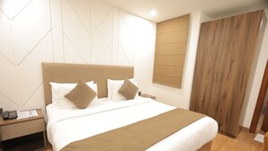 Una cama bien tendida con una manta marrón, una mesita de noche de madera con un teléfono y papeles, y un armario de madera.