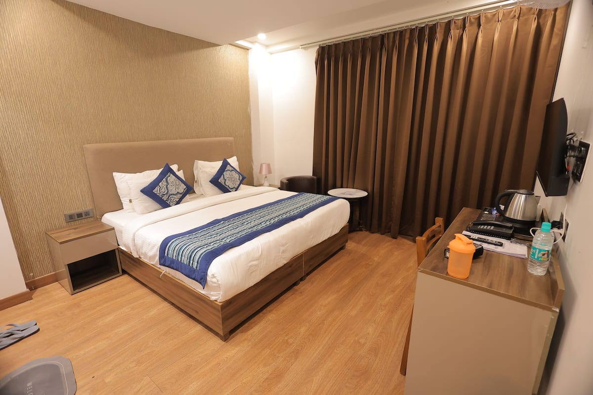 A hotel room with a bed, bedside table, and a desk with a water bottle and remote controls.