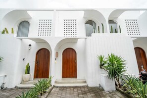 A white building with three wooden doors, each with a small porch and potted plants. - Villa Casa Zaya A (Canggu)