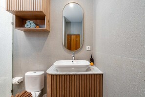 A bathroom with a wooden vanity, a white sink, a toilet, and a mirror. - Villa Casa Zaya A (Canggu)