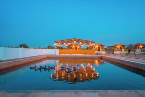 A pool with ducks, a covered seating area, and a building with multiple rooms. - Vijay Bagh Thar Village Resort (Jaisalmer)