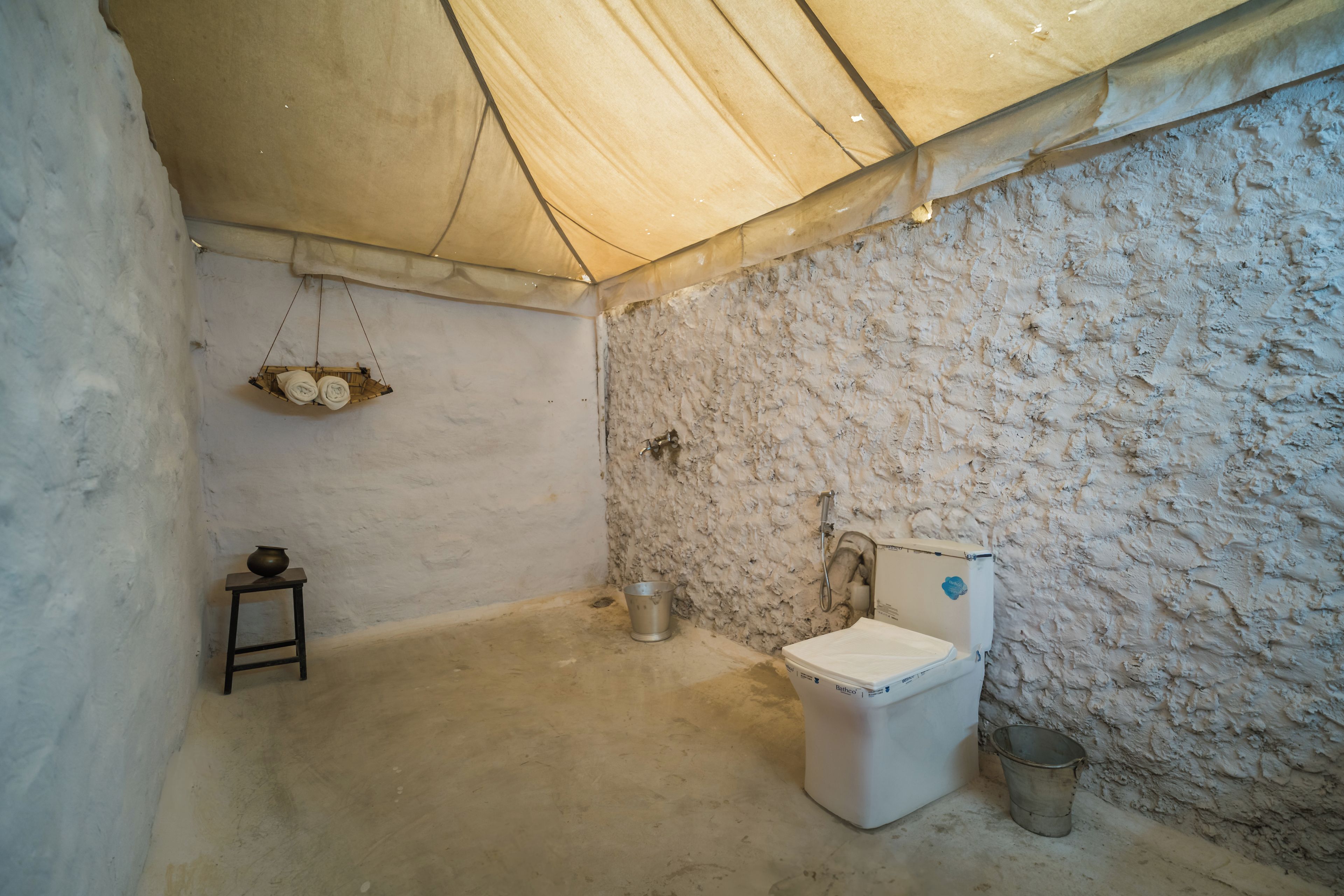 Una habitación con carpa, un inodoro, una mesita con una olla y un balde.