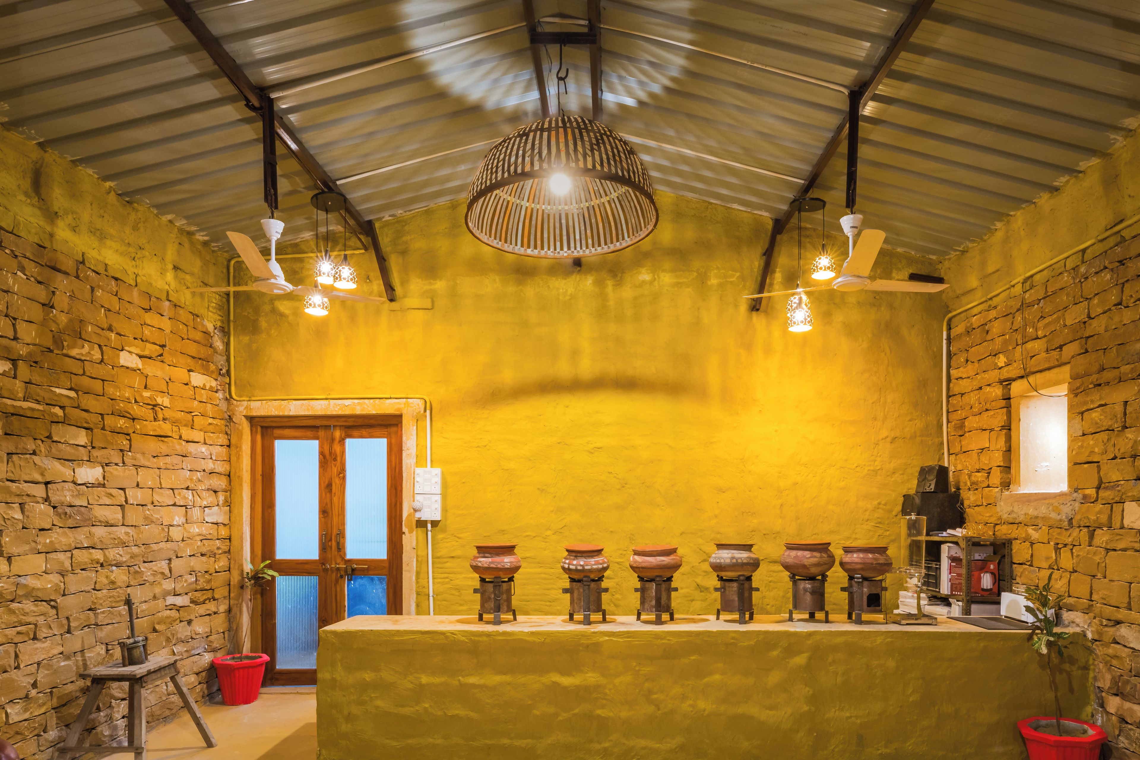 Une pièce avec un mur en pierre, une porte en bois, un ventilateur de plafond et une table ornée de poteries.