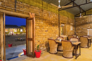 An indoor dining area with brick walls, wooden furniture, and a view of the outside. - Vijay Bagh Thar Village Resort (Jaisalmer)
