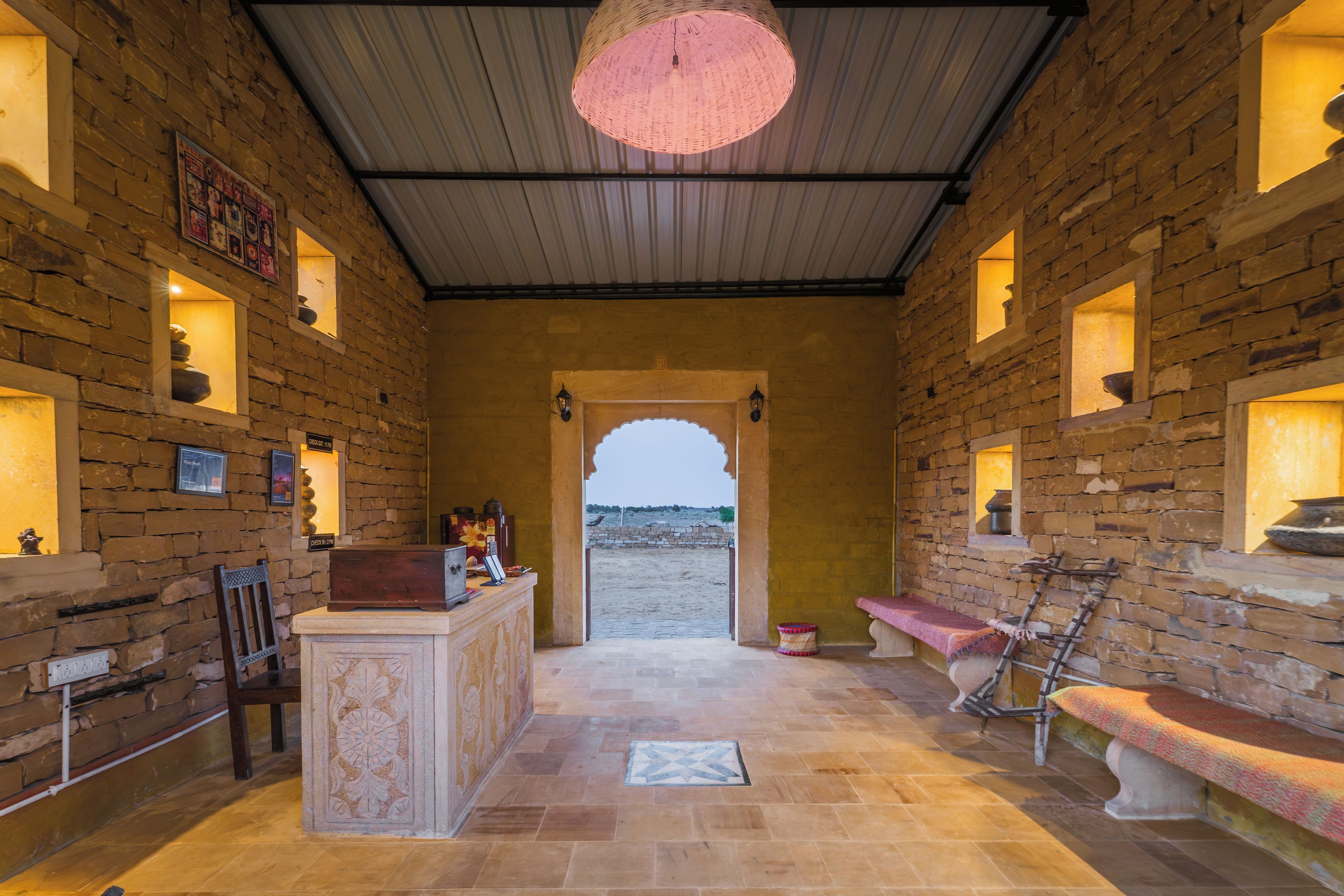 A stone-walled interior with a central reception desk, a bench, and a view through an archway to the outside.