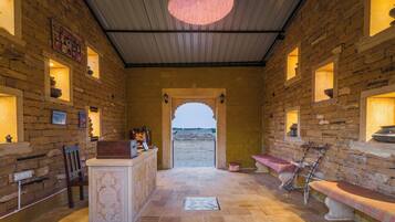 A stone-walled interior with a central reception desk, a bench, and a view through an archway to the outside.
