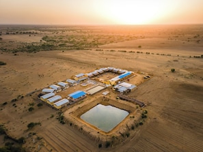An aerial view of a rural settlement with multiple buildings, a central water body, and surrounding fields. - Vijay Bagh Thar Village Resort (Jaisalmer)