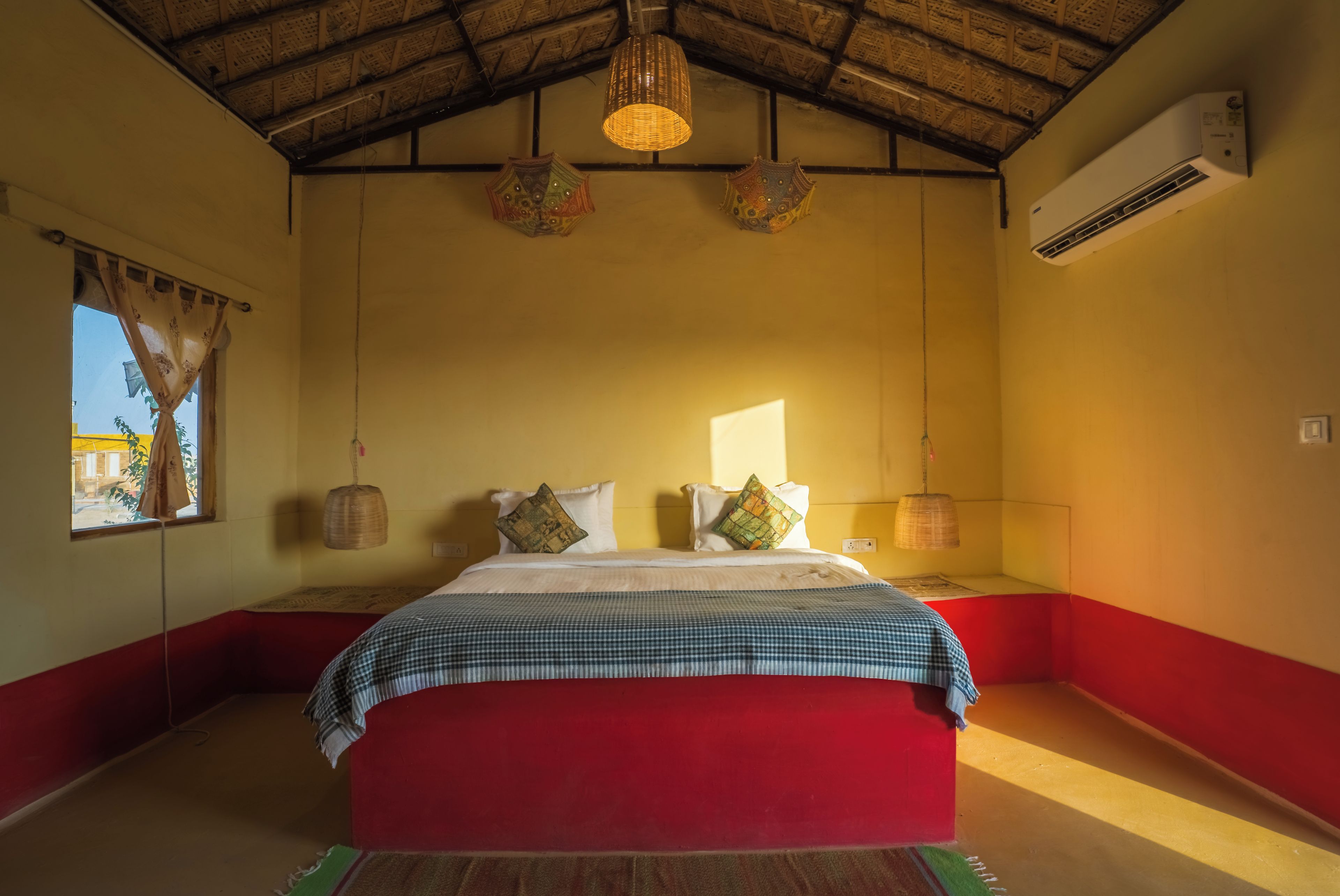 Una habitación con cama, ventana con cortinas, lámpara colgante y aire acondicionado.