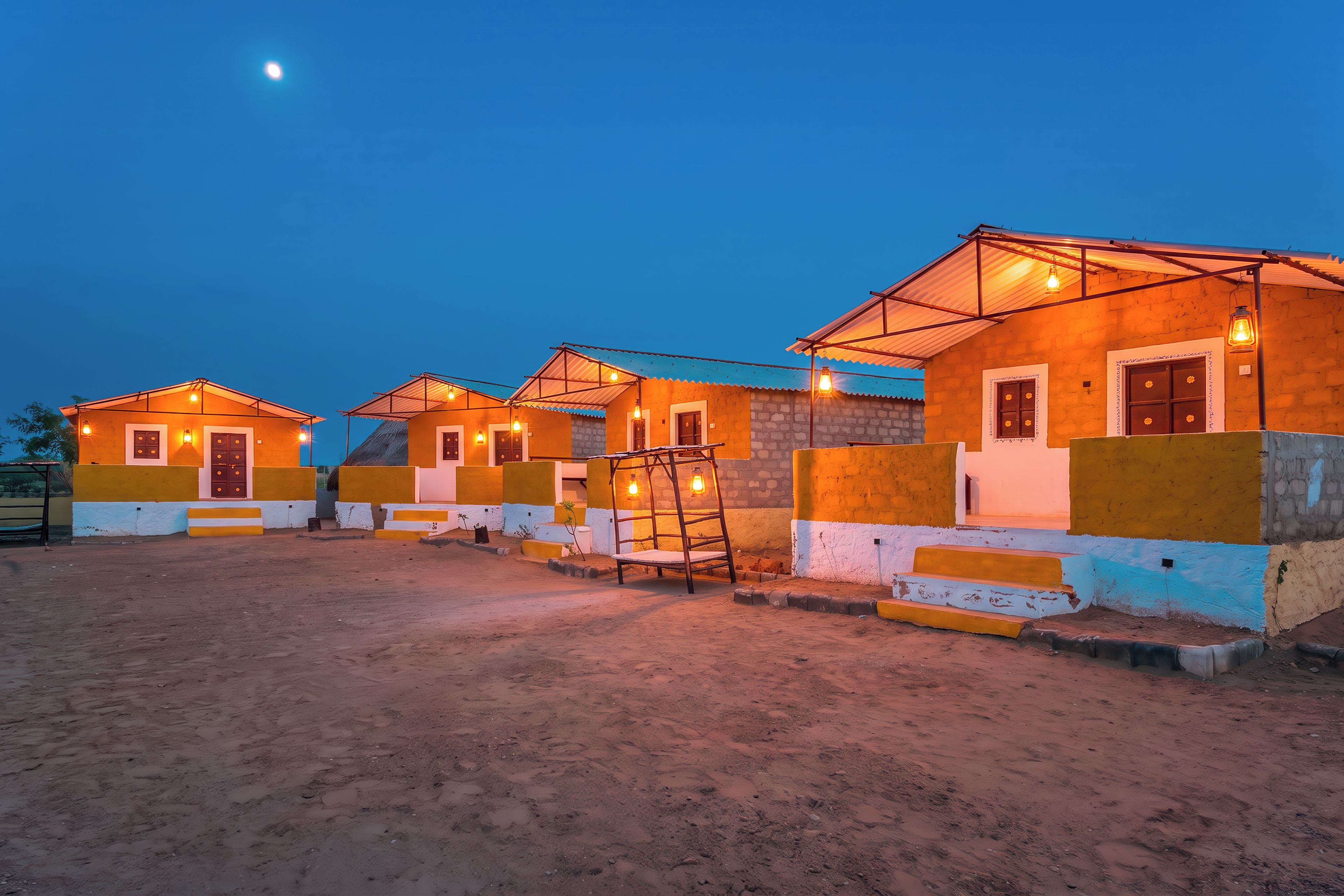 A row of small, brightly lit cottages with a dirt ground in front.
