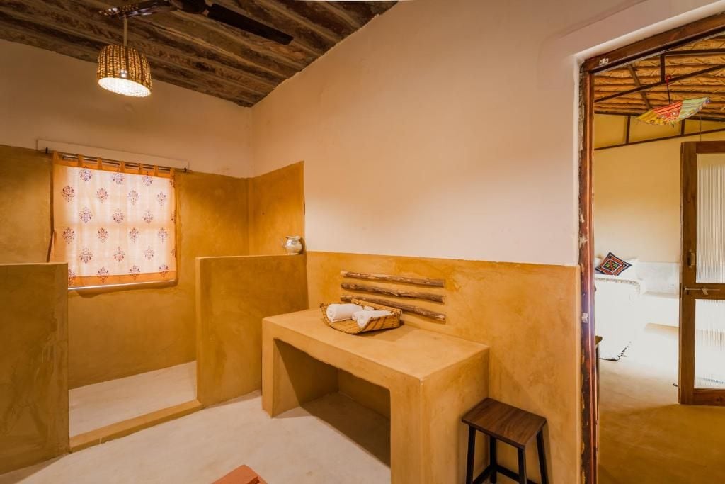A bathroom with a wooden bench, a small table, and a window with patterned curtains.