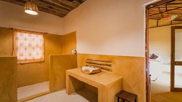 A bathroom with a wooden bench, a small table, and a window with patterned curtains.