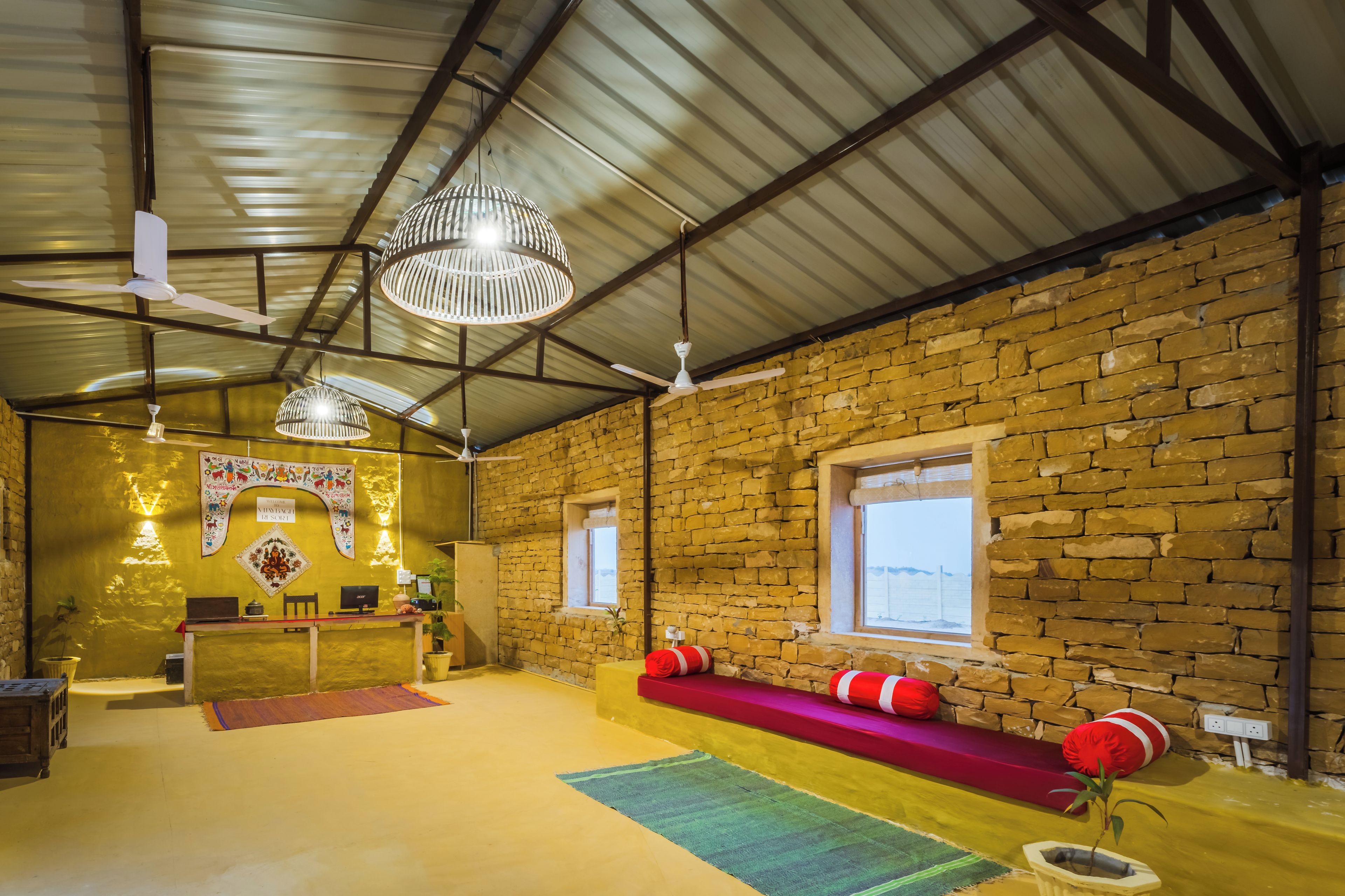 A rustic interior with a stone wall, a reception desk, a bench with red cushions, and a ceiling fan.
