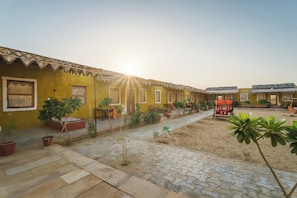 A courtyard with yellow buildings, potted plants, and a patterned stone floor. - Vijay Bagh Thar Village Resort (Jaisalmer)