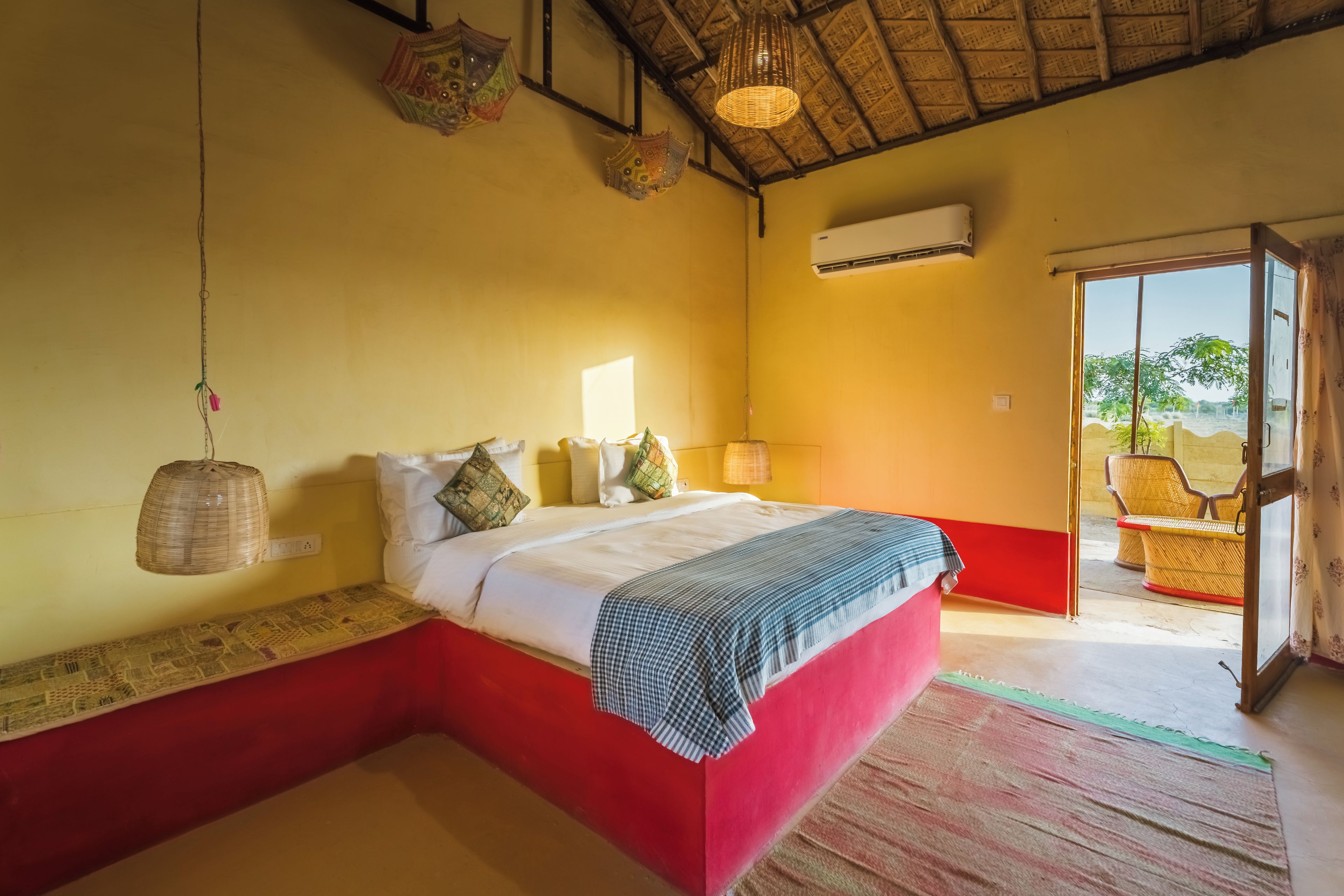 Une chambre à coucher avec un lit, une lampe de chevet, un luminaire suspendu et une vue sur l’extérieur par une porte ouverte.