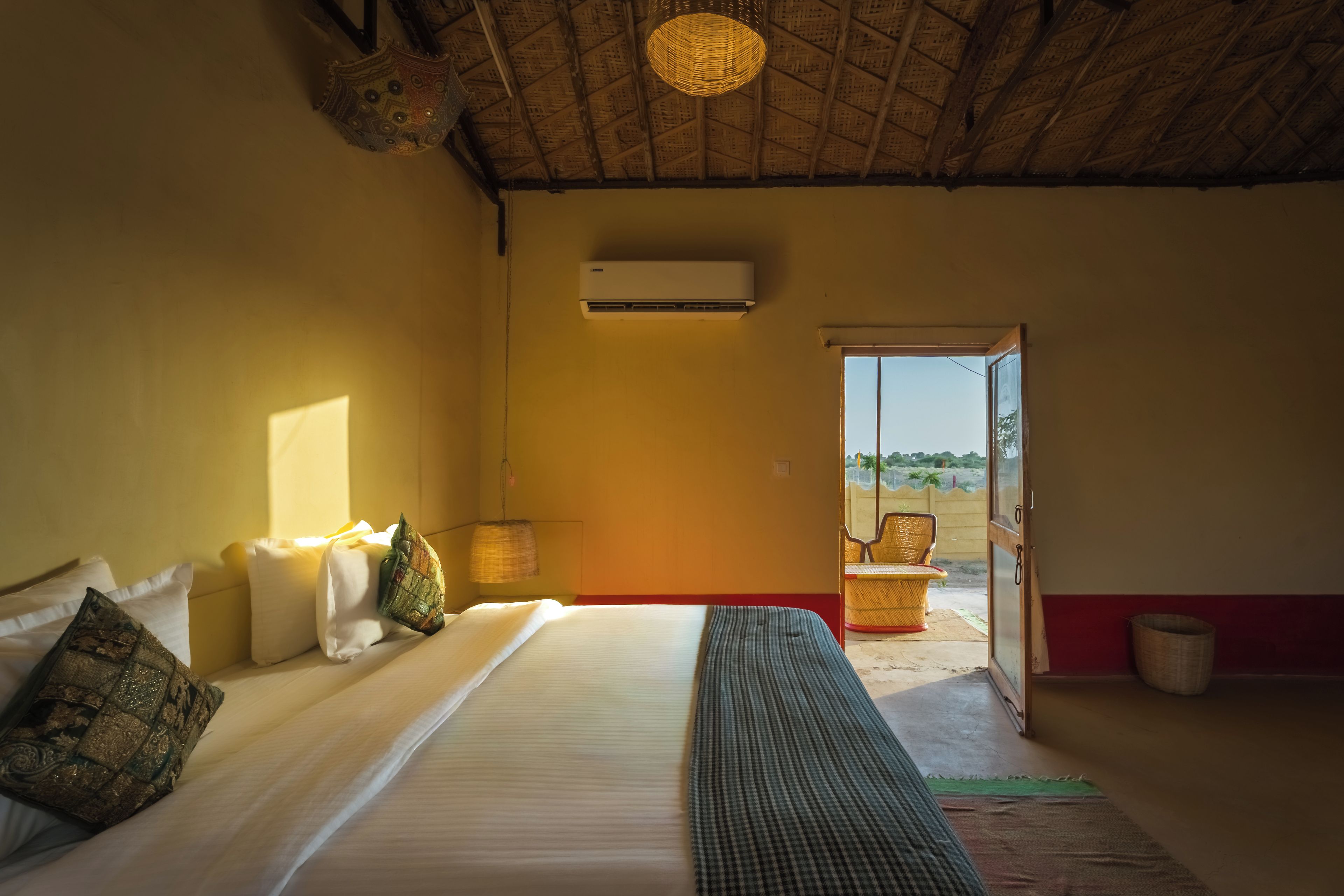 A room with a bed, a window, an air conditioning unit, and a view of the outside.