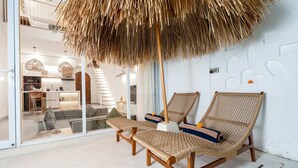 A modern interior with wicker lounge chairs, a thatched ceiling, and a view of a kitchen and living area. - Villa Casa Zaya B (Canggu)