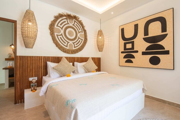 A bedroom with a large bed, wooden paneling, two hanging light fixtures, and a wall art piece. - Villa Jacelyne (Canggu)