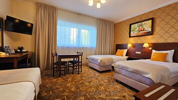 Habitación de hotel con dos camas, una mesa de comedor, sillas, televisor y un cuadro en la pared.