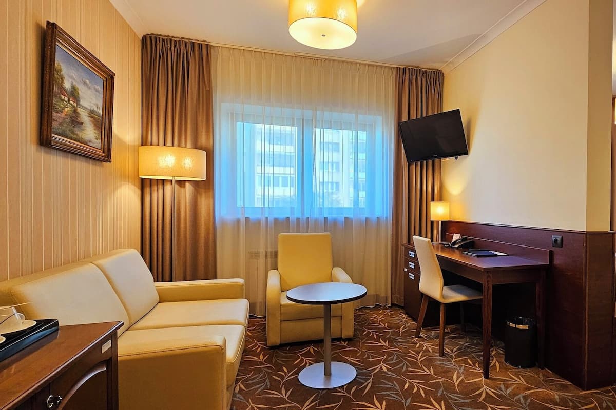 Hotellihuone, jossa on sänky, työpöytä, tuoli, sohva ja televisio.