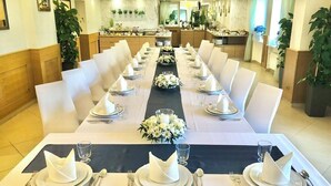 Una larga mesa de comedor dispuesta para una comida formal, con manteles blancos, servilletas dobladas con cuidado y cristalería.