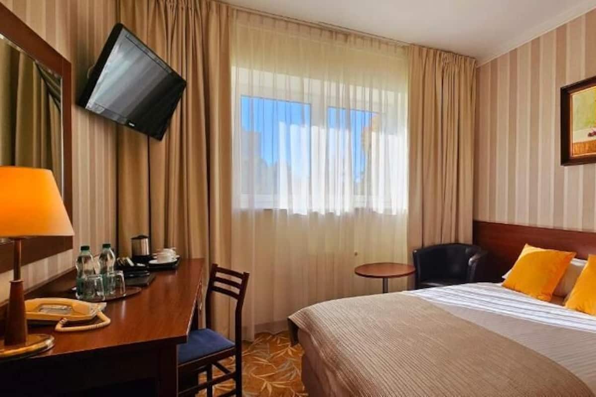 Hotellihuone, jossa on sänky, kirjoituspöytä, jossa on puhelin, tuoli, pieni pöytä ja seinälle asennettu televisio.