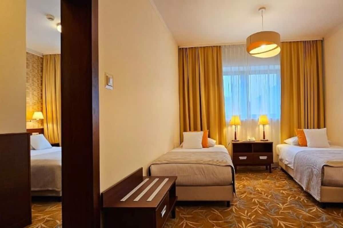 Hotellihuone, jossa on kaksi erillistä sänkyä, sohva, pieni pöytä ja tuoli.