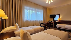 Habitación de hotel con dos camas individuales, un escritorio con silla, televisión y ventana con cortinas.