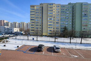 A parking area with two cars, a brick pavement, and a fence. - Centrum Barnabitów (Warsaw)