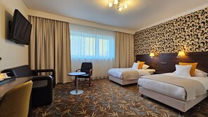 A hotel room with two beds, a desk, a chair, a TV, and a patterned carpet. - Centrum Barnabitów (Warsaw)
