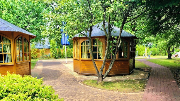 Un parque con gazebos de madera, senderos pavimentados y abundante vegetación.