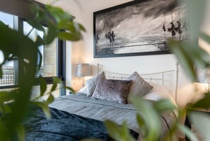 Quarto com cama, almofadas, mesa de cabeceira, luminária e um quadro na parede.