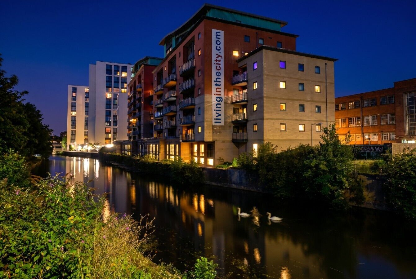 Een hotel met meerdere verdiepingen en balkons, met een rivier ervoor, en een bord met de website.