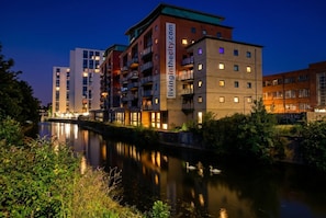 A multi-story hotel with balconies, a river in front, and a website sign. - Cosy Flat with River-view balcony, free secure parking, and city centre location (Leicester)