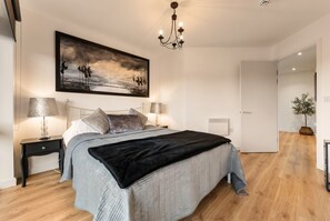 A bedroom with a bed, two bedside tables, a chandelier, a painting, and a door leading to another room. - Cosy Flat with River-view balcony, free secure parking, and city centre location (Leicester)