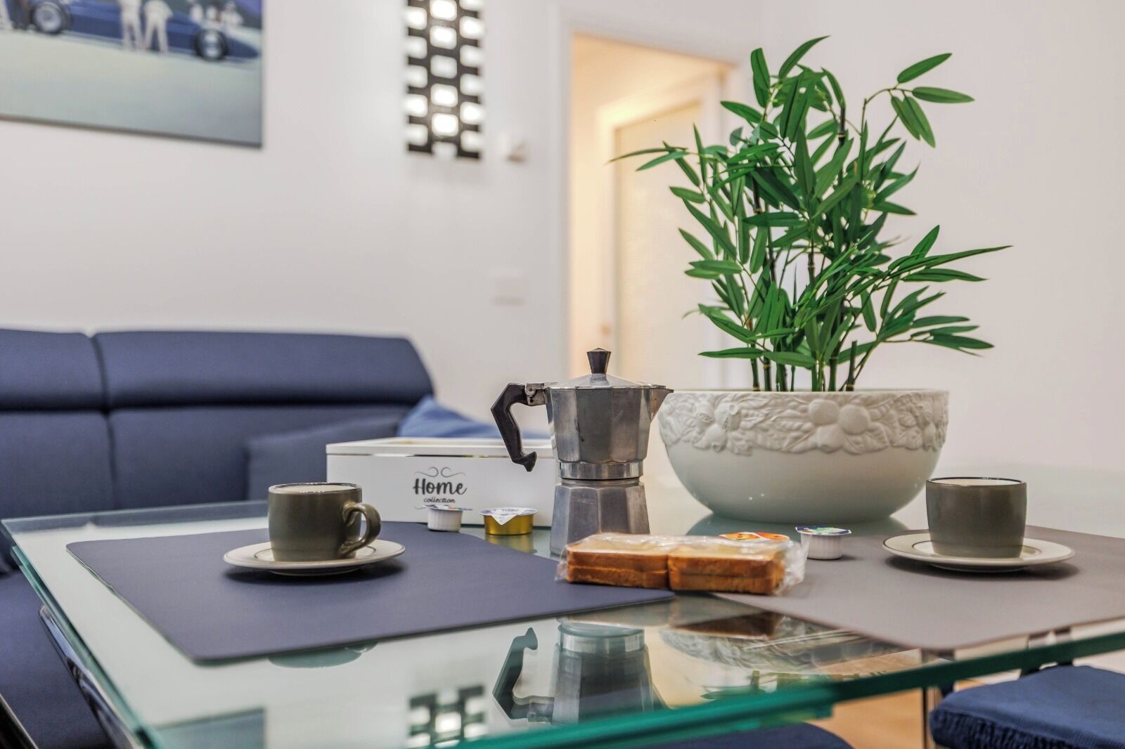 Ett modernt vardagsrum med ett soffbord i glas, två kaffekoppar, en dekorativ skål och en växt.