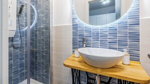 Een moderne badkamer met een douchecabine van glas, een ronde spiegel en een houten wastafelmeubel met een wit waskom.
