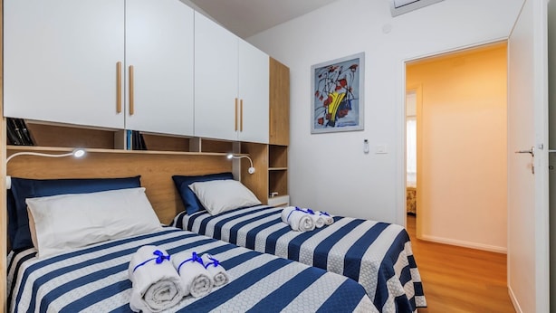Een slaapkamer met twee bedden, elk met gestreept beddengoed en opgerolde handdoeken. Er is een houten hoofdbord, een wandplank en een schilderij boven de bedden.