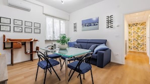 Een moderne woonkamer met een glazen eettafel, een blauwe bank en een houten dressoir.