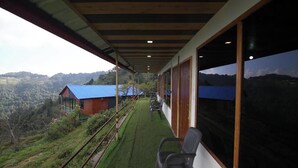 Un balcon donnant sur un paysage montagneux, un petit bâtiment avec un toit bleu et une rangée de chaises.