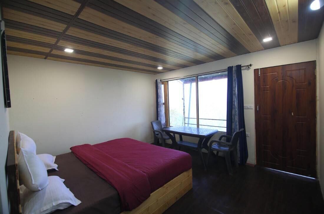 A room with a bed, a table, and chairs, a window with curtains, and a wooden door.