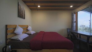 Un lit simple avec une tête de lit en bois, une couverture rouge et des oreillers blancs. Il y a une petite table et une chaise sur la droite.