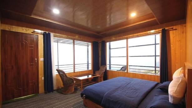 Une pièce en bois avec un lit, deux chaises, une table et de grandes fenêtres.
