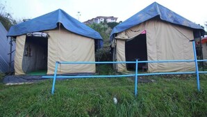 Deux tentes recouvertes de bâches bleues, un portail en métal et une zone herbeuse.