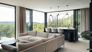A modern living room with a sofa, a dining area with chairs, and a view of cacti and greenery through large windows. - Villa Solara Cove Modern Design Luxury Nature (Sint Willibrordus)