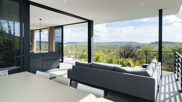 A modern outdoor living space with a sofa, dining table, and a view of a mountainous landscape. - Villa Solara Cove Modern Design Luxury Nature (Sint Willibrordus)