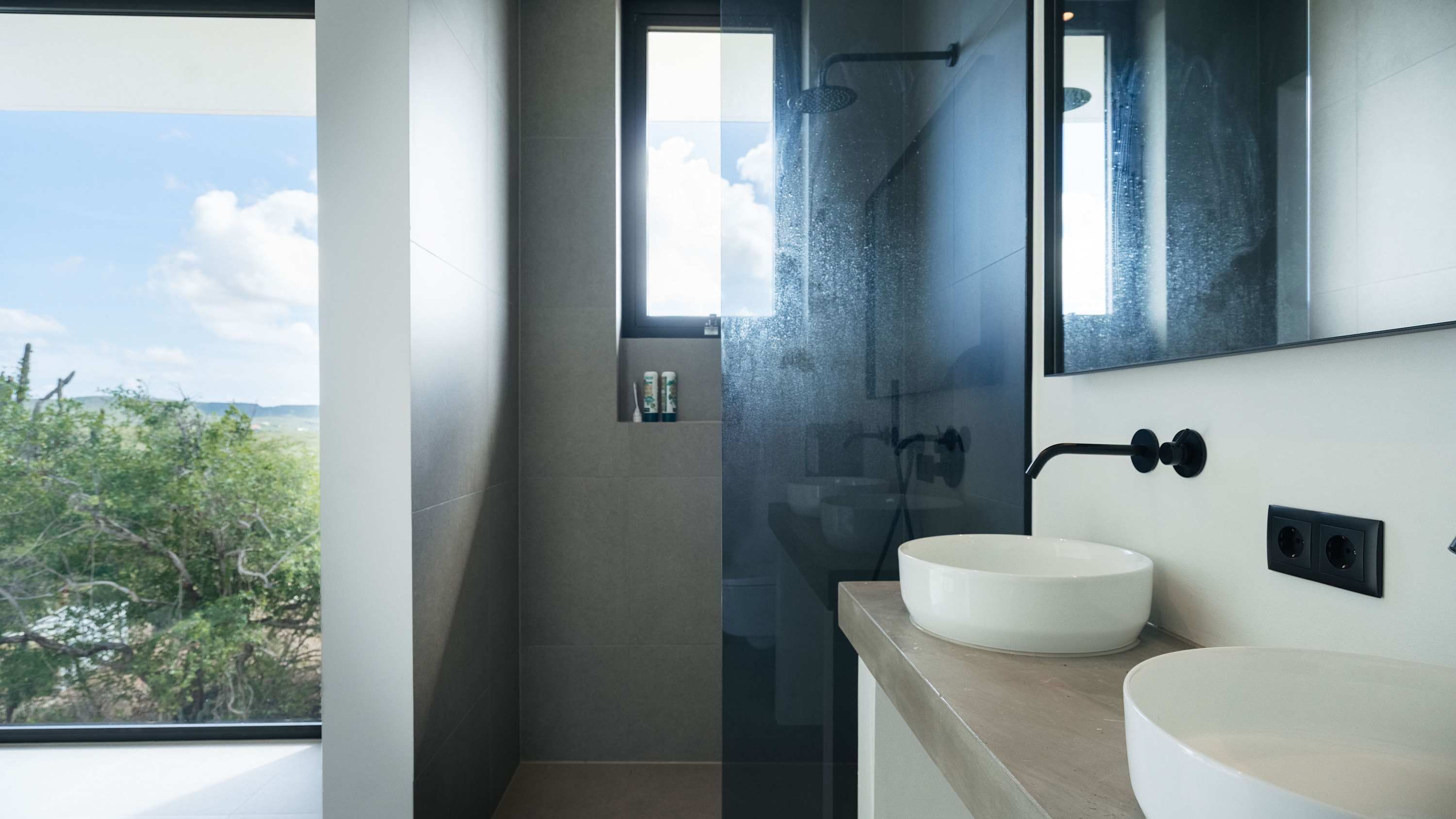 A modern bathroom with a large window, two sinks, and a shower.