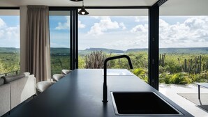 A modern kitchen with a large window, a sink, and a dining area with a sofa. - Villa Solara Cove Modern Design Luxury Nature (Sint Willibrordus)